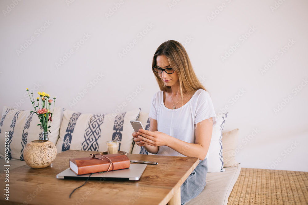 Pensive caucasian female in casual wear sitting in cozy home interior using mobile phone for chatting and sending text messages, serious hipster girl 20s checking notification from social networks Pensive caucasian female in casual wear sitting in cozy home interior using mobile phone for chatting and sending text messages, serious hipster girl 20s checking notification from social networks