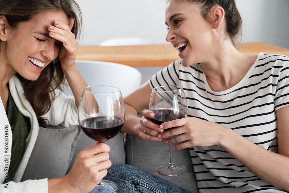 Two friends laughing with a glass of wine in hand Two friends laughing with a glass of wine in hand