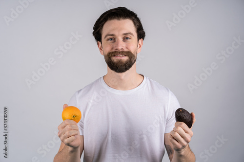 Man with long beard shows avocado and orange. Fruit and healthy organic food. Dieting and fitness.