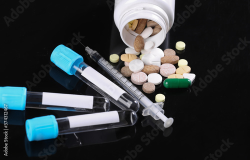 Medical test tubes and syringe, pills isolated on black background photo