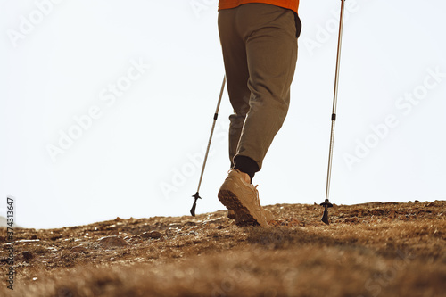 Man traveler with trekking sticks going up the mountain