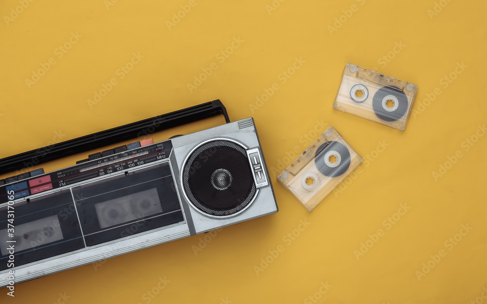 Fototapeta premium 80s Retro outdated portable stereo radio cassette recorder and audio cassette on yellow background. Top view