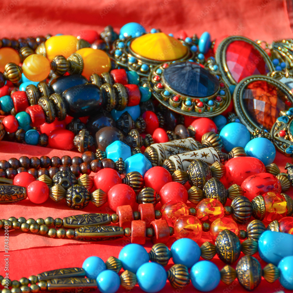 The necklace is carved from ivory, carved brass, round, with stones, stones, many colorful, handmade, tied in a beautiful necklace, arranged on a red cloth. The necklace is carved from ivory, carved brass, round, with stones, stones, many colorful, handmade, tied in a beautiful necklace, arranged on a red cloth.