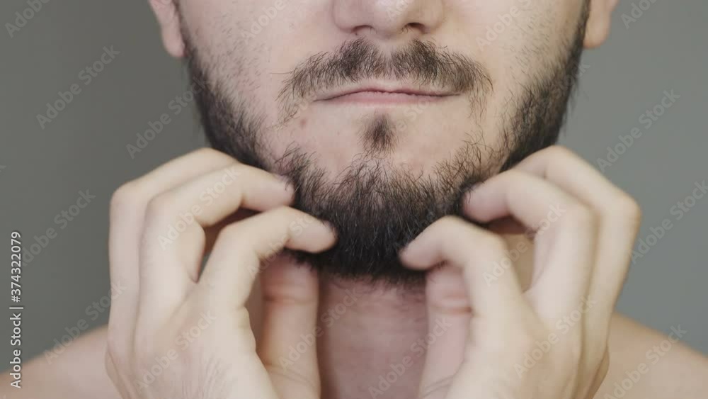 Young man touches his stubble of beard. A Caucasian man strokes his unshaven face. Unshaven male face close-up. Young man touches his stubble of beard. A Caucasian man strokes his unshaven face. Unshaven male face close-up.
