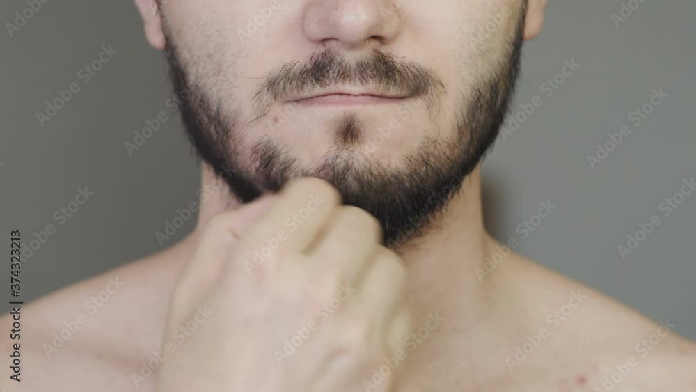Young man touches his stubble of beard. A Caucasian man strokes his unshaven face. Unshaven male face close-up. Young man touches his stubble of beard. A Caucasian man strokes his unshaven face. Unshaven male face close-up.