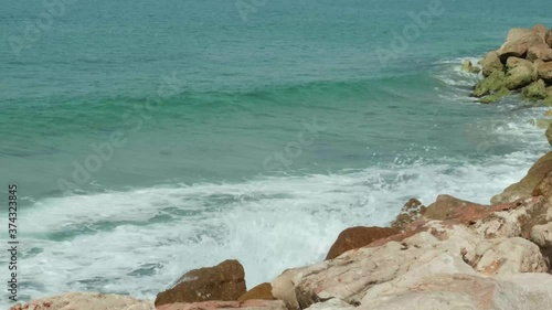 Wide shot of blue and green waves of a beautiful sea crushing onto stones of a sea shore. Slow motion 4K