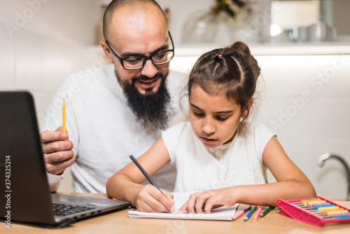 Father helping daughter with homework using digital notebook.
