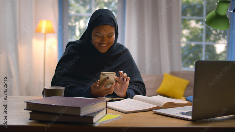 Muslim female student learning at home surfing internet on smartphone Muslim female student learning at home surfing internet on smartphone