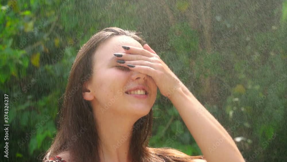A young woman rejoices in the summer rain. Woman raises her head up and smiles. Slow motion A young woman rejoices in the summer rain. Woman raises her head up and smiles. Slow motion