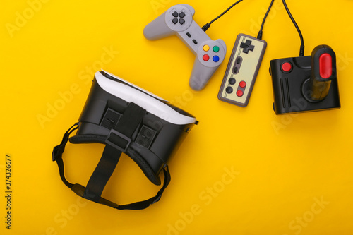 Virtual reality headset, retro gamepads and joystick on yellow background. Entertainment, 3d video game. Top view