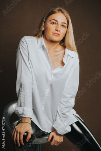 An attractive caucasian blonde female in a white shirt posing on a brown background

