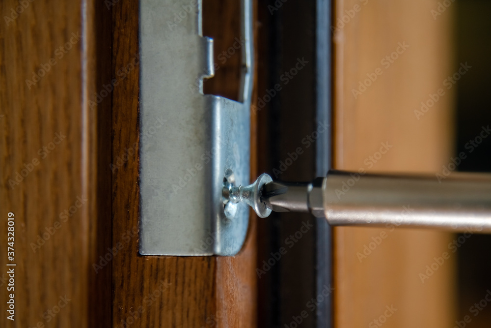 Close up of carpenter repairing door lock. Installing a door handle. Handyman tightening door hinge . Hands of the repairman with a screwdriver. Locksmith screwing bolt into wooden door Close up of carpenter repairing door lock. Installing a door handle. Handyman tightening door hinge . Hands of the repairman with a screwdriver. Locksmith screwing bolt into wooden door