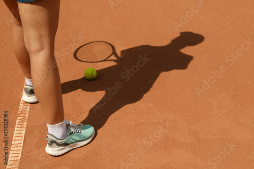 Woman in sneakers on clay court with tennis ball