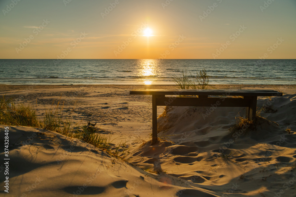 Empty wooden bench and beautiful golden sunset at the beach. Sun setting into the sea on tranquil evening. Nobody