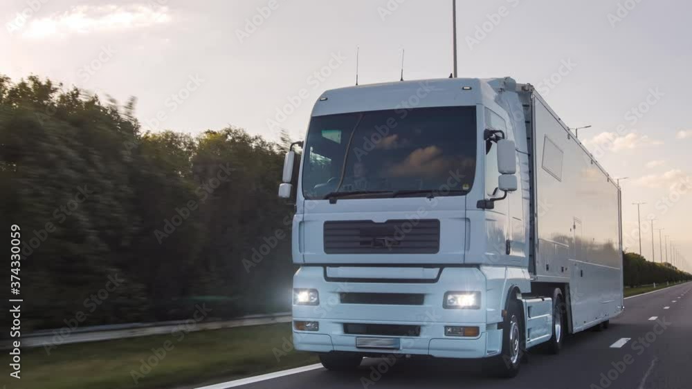 Cargo truck with cargo trailer driving on a highway. White Truck delivers goods in early hours of the Morning - very low angle drive thru close up shot. Cargo truck with cargo trailer driving on a highway. White Truck delivers goods in early hours of the Morning - very low angle drive thru close up shot.