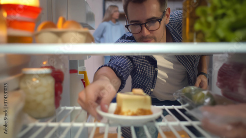 Hungry man looking for a snack in fridge taking piece of cake
