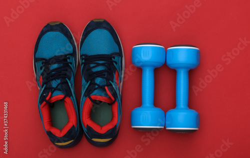 Sports shoes (sneakers) and blue dumbbells on red background. Healthy lifestyle, fitness training. Top view