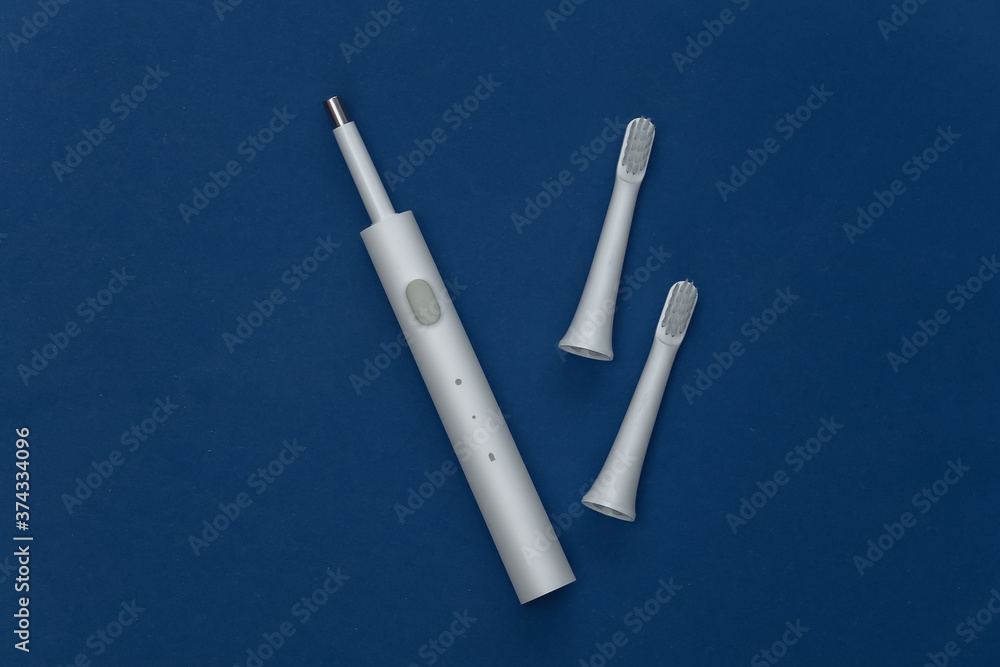 Obraz premium Electro toothbrush with replaceable heads on classic blue background. Color 2020. Top view