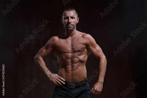 Slim athletic man with a naked muscular torso isolated on a dark background.