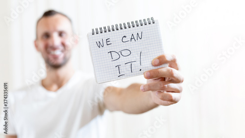 blurred man holds in his outstretched hand a sheet of paper with the inscription WE CAN DO IT with copy space