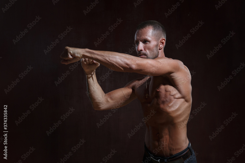 Charismatic athletic male fighter with muscular torso strikes isolated on dark background.
