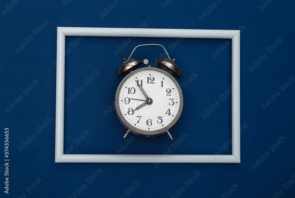 Retro alarm clock on classic blue background with white frame. Color 2020. Top view Retro alarm clock on classic blue background with white frame. Color 2020. Top view