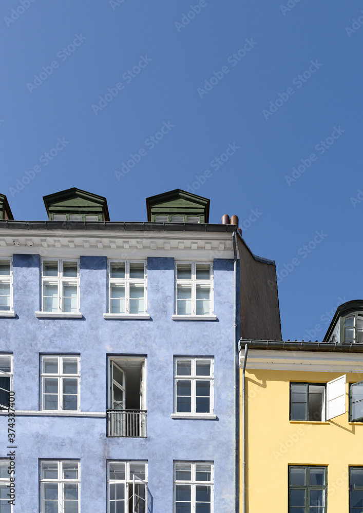 Colorful houses in yellow and blue of the Nyhaven in Copenhagen Denmark photographed frontally on a sunny day with a bright blue sky.