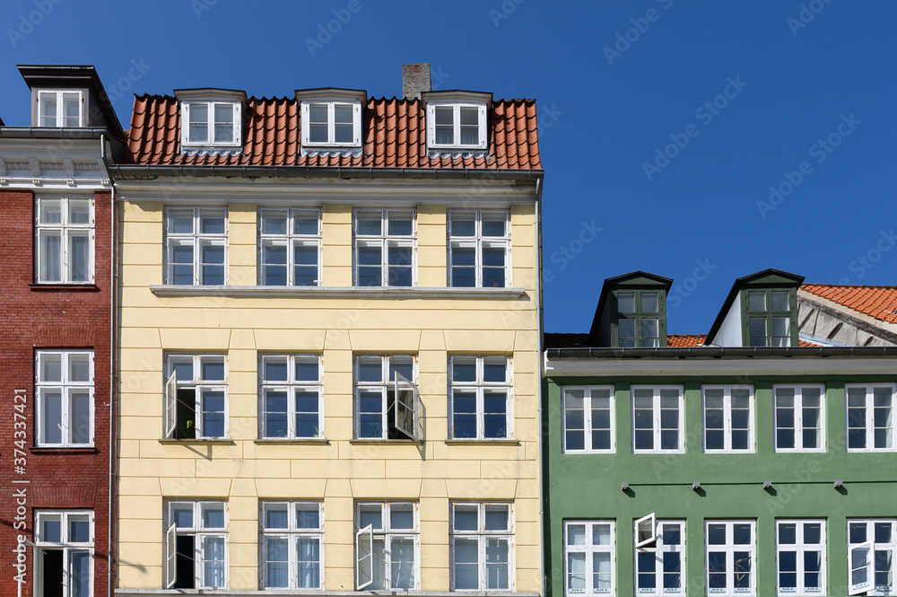 Colorful houses in brown, yellow and green of the Nyhaven in Copenhagen Denmark photographed frontally on a sunny day with a bright blue sky.