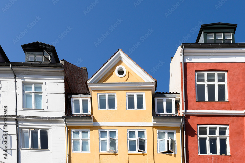 Colorful houses in red, yellow and white of the Nyhaven in Copenhagen Denmark photographed frontally on a sunny day with a bright blue sky.