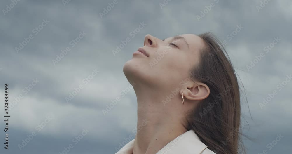 Close up portrait of female face looking up into stormy sky copy text space handheld device. Young woman posing on nature background outdoors slow motion. Trust hope love concept. Facial care