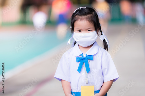 Female student wearing white mask goes to school. Asian girl wear mask to prevent the outbreak of new corona virus and to prevent dust. Student look at camera. She wears blue and white school uniform.