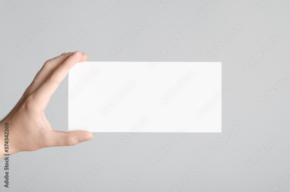 Obraz premium DL Flyer Mock-Up - Male hands holding a blank flyer on a gray background.