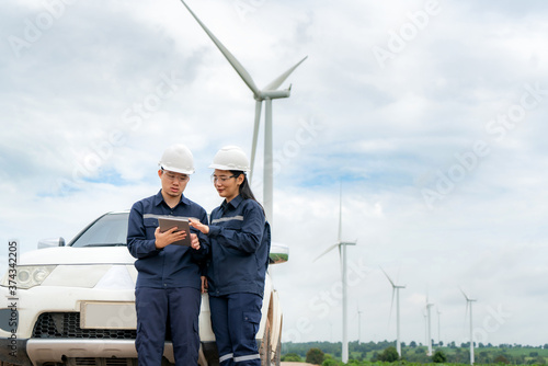 Asian man and woman Inspection engineers preparing and progress check with digital tablet of a wind turbine with safety in wind farm in Thailand.