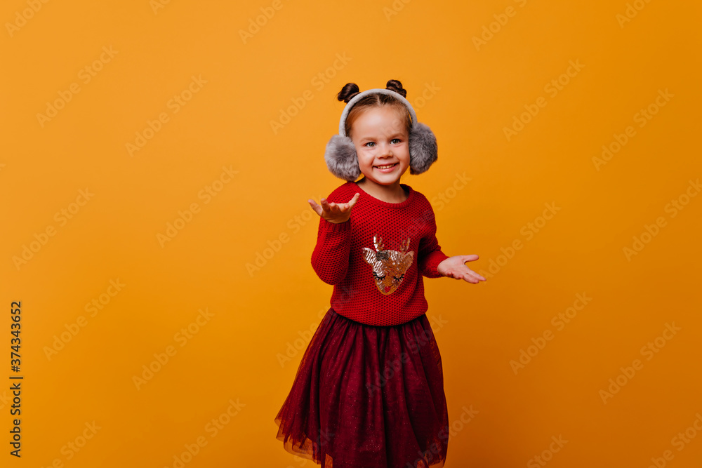 little girl is dancing incendiary dance in a bright, beautiful sweater with Christmas shiny deer. Baby in gray headphones on isolated background