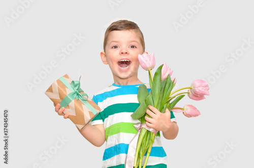 A cute little boy gentleman in a colored striped t-shirt holding a bouquet of pink tulips and a gift box with a green bow.