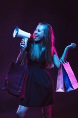 Shouting with shopping bags for sales. Portrait of young woman in neon light on dark backgound. The human emotions, black friday, cyber monday, purchases, sales, finance concept.