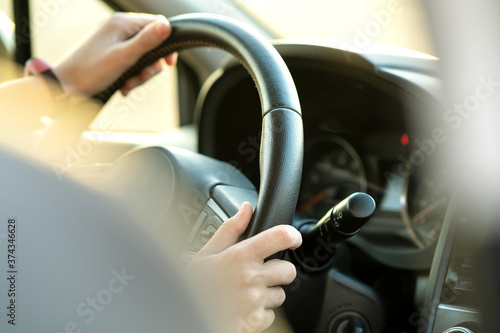 Close up view of woman hands holding steering wheel driving a car on city street on sunny day.