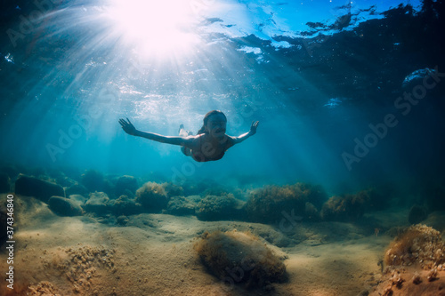 Attractive woman dive near stone with seaweed in underwater. Swimming in ocean
