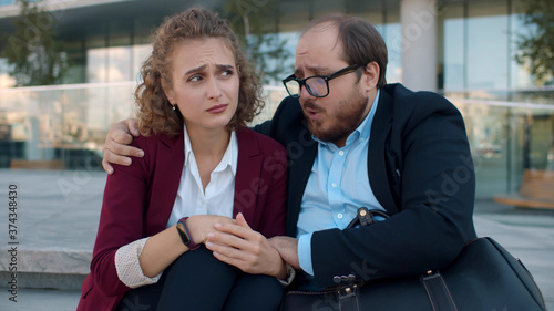 Fototapeta Naklejka Na Ścianę i Meble -  Overweigh male colleague comforting depressed sad young woman sitting on stairs outdoors