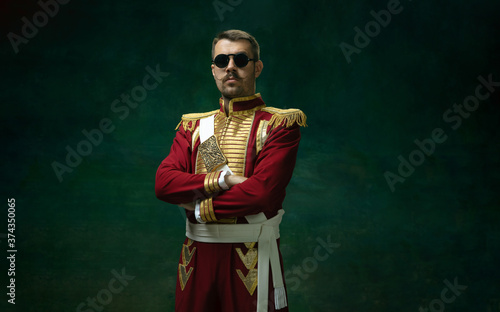 Wearing stylish eyewear. Young man in suit as Nicholas II isolated on dark green background. Retro style, comparison of eras concept. Beautiful male model like historical character, monarch, old photo