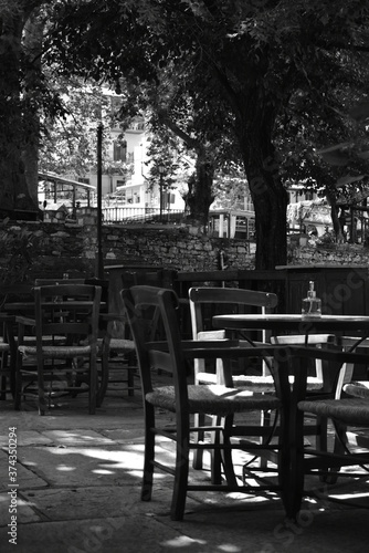 table and chairs in a cafe  in the central square of a village   black   white 