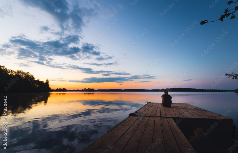 Person sitting on dock at sunset