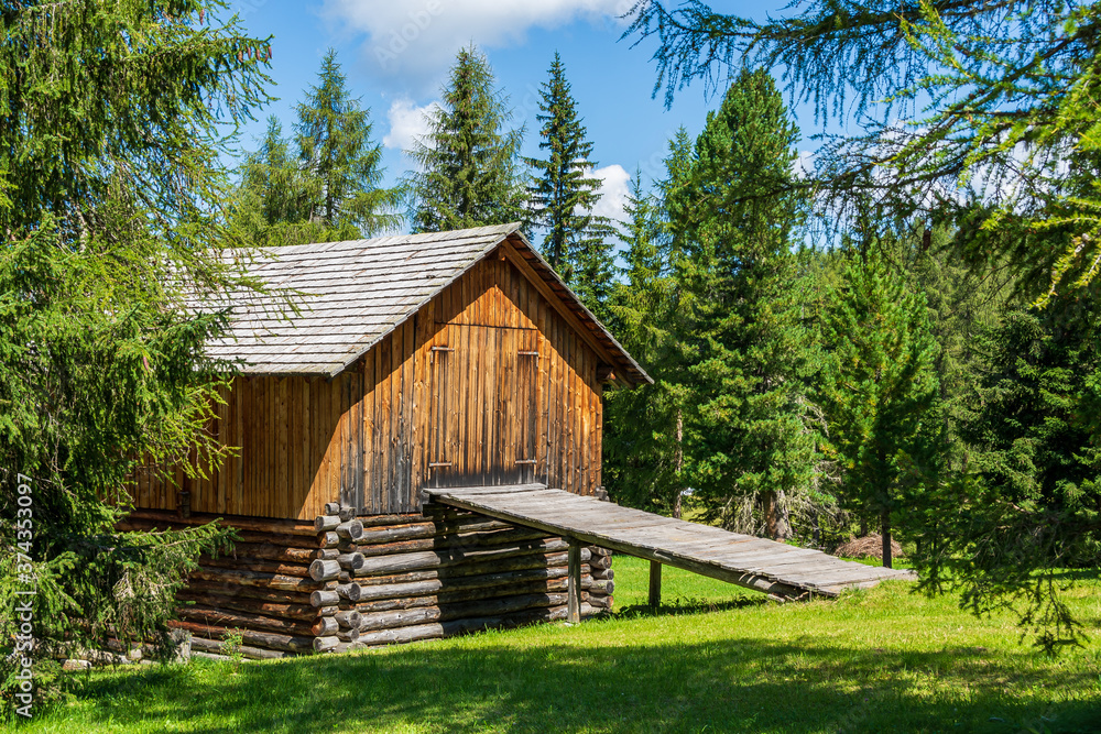 Isolated mountain hut made of wood surrounded by green meadows and fir trees during summer. Val Badia - South Tyrol, Italy Isolated mountain hut made of wood surrounded by green meadows and fir trees during summer. Val Badia - South Tyrol, Italy