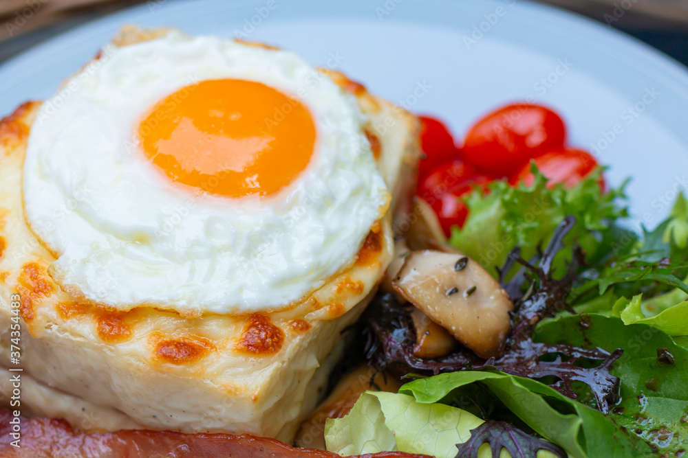 Croque madame delicious breakfast with ham, cheese, egg and spinach with vegetables. Cut fried egg on Croque madame, ham and cheese closeup on the plate. Eating croque-madame with beautiful fried egg. Croque madame delicious breakfast with ham, cheese, egg and spinach with vegetables. Cut fried egg on Croque madame, ham and cheese closeup on the plate. Eating croque-madame with beautiful fried egg.