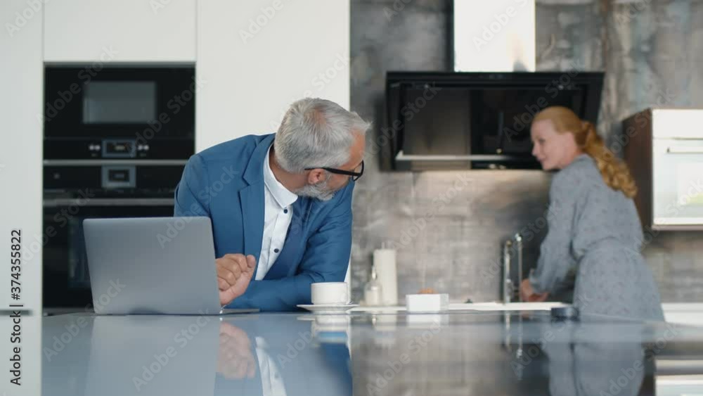 Senior businessman working on laptop and having coffee for breakfast in kitchen Senior businessman working on laptop and having coffee for breakfast in kitchen