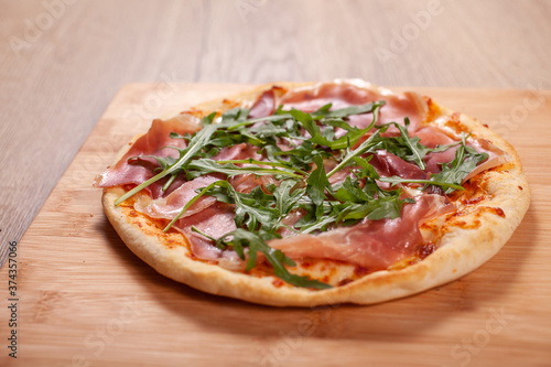 Pizza with prosciutto, cheese and arugula on wooden board