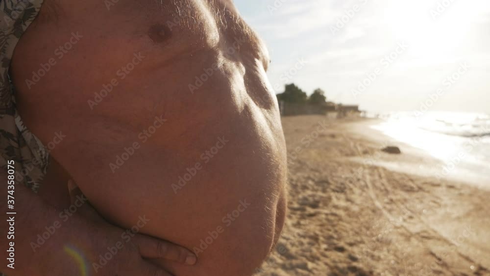 Close-up of a man's big belly on the beach, with a cross on his neck Close-up of a man's big belly on the beach, with a cross on his neck