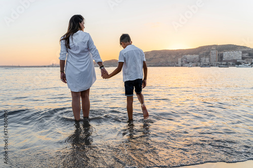 Woman and son standing in the sea holding hands watching a sunset.