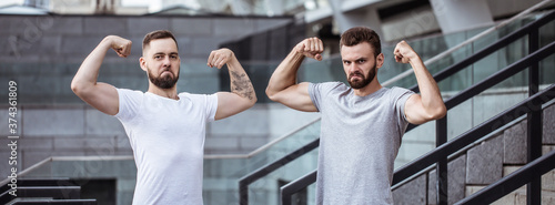 Two happy funny excited handsome bearded best friends in casual t-shirts are showing biceps on camera and having fun. Sport  fitness  strong men  power in the team.