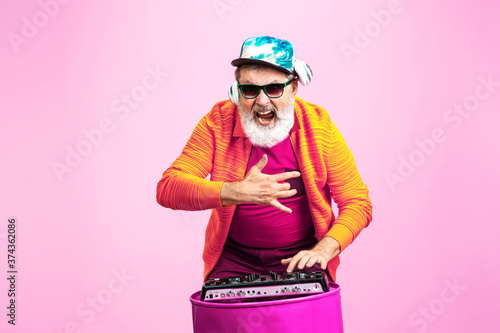 DJ. Portrait of senior hipster man in fashionable eyewear isolated on pink studio background. Tech and joyful elderly lifestyle concept. Trendy colors, forever youth. Copyspace for your ad.